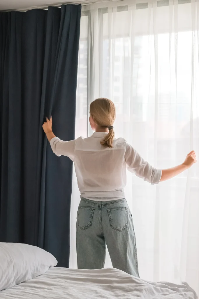 The 9 Best Blackout Curtains for Athletes to Maximize Recovery and Deep Sleep Woman puting on blackout curtains